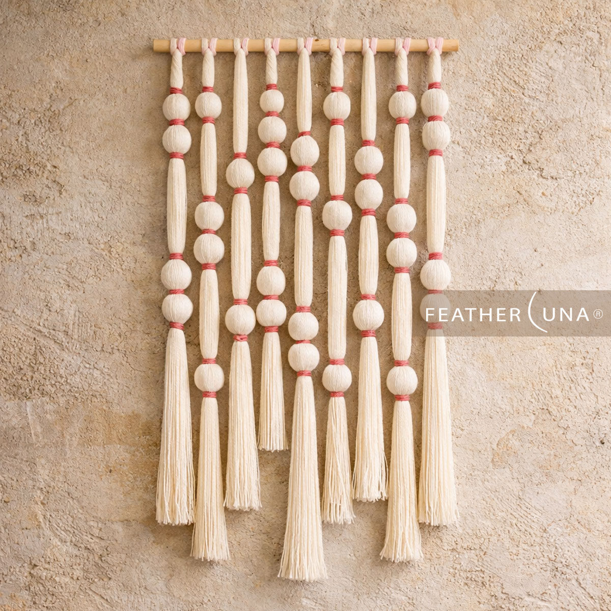 Cotton cord wall hanging of wrapped beads, pink bands and long tassels on a wooden rod