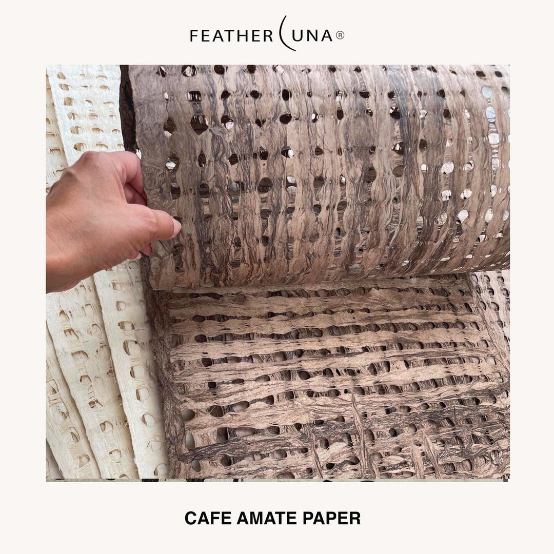A hand unrolling a sheet of Café amate paper, with Crème sheets beside it