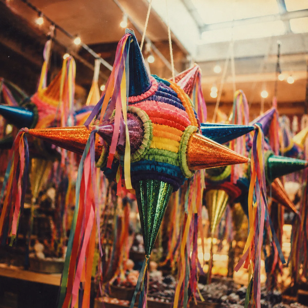 A pinata de siete picos with seven cones and trailing tissue streamers hanging in an artisan workshop