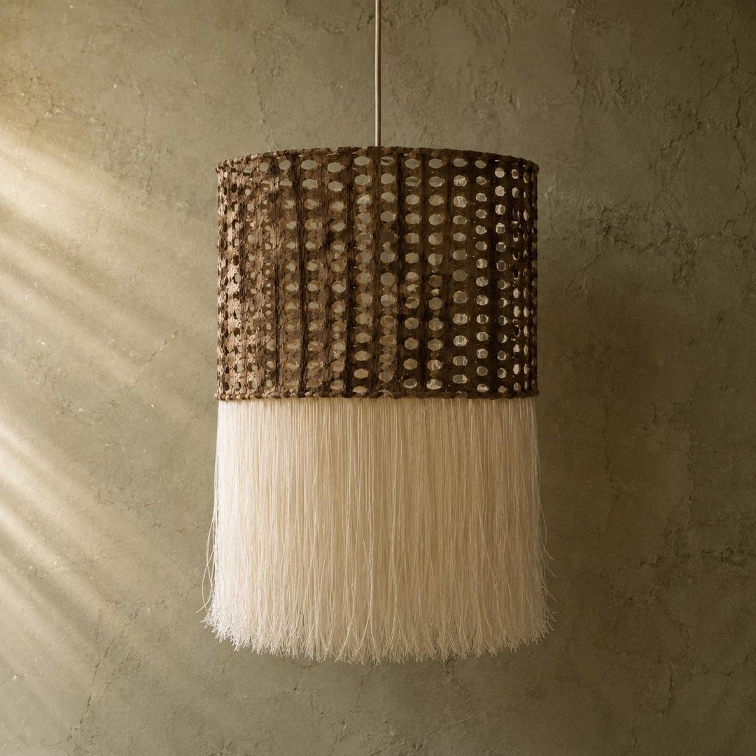 A hanging drum of Café amate paper with a long cream cotton fringe, against a green plaster wall