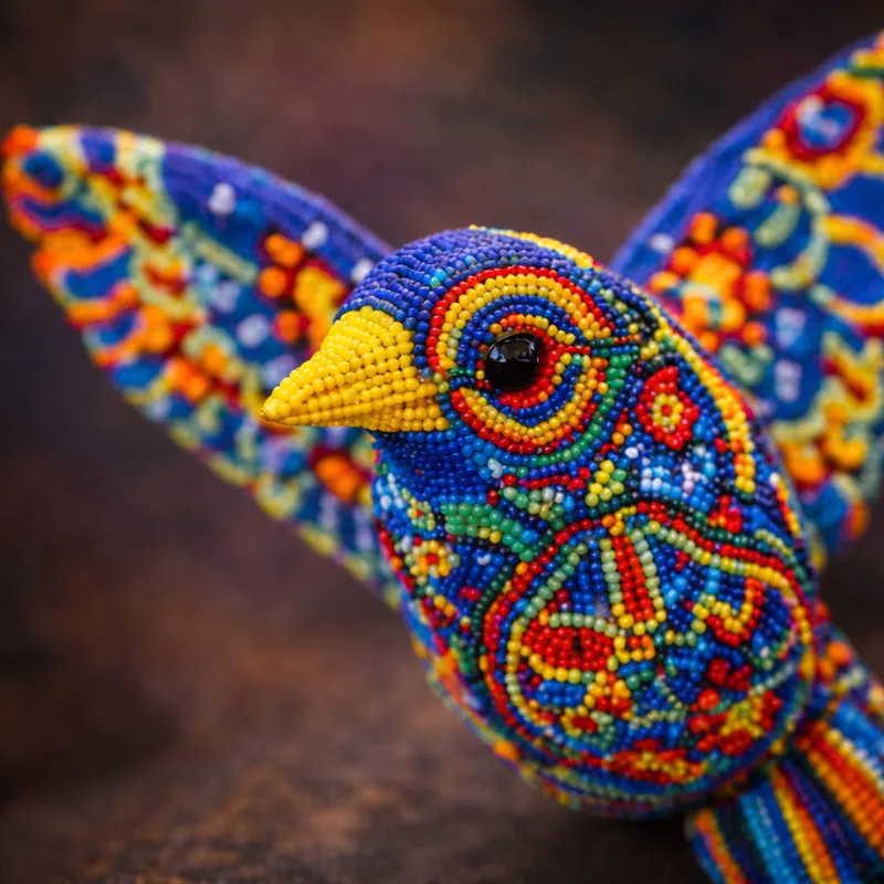 A beaded bird figure with wings spread, entirely scaled in glass beads arranged in a symmetrical flower-star pattern on both wings.